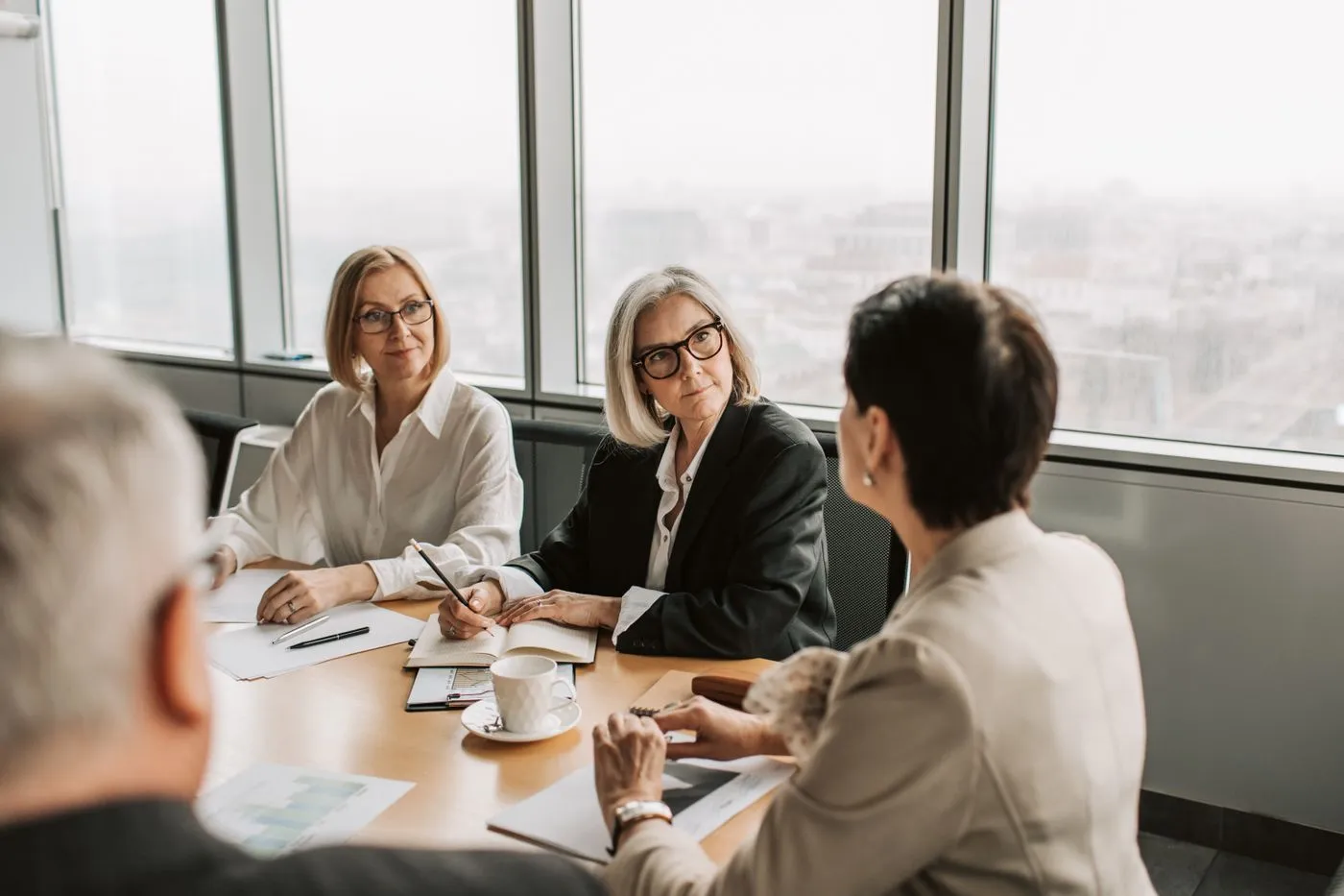 Quatre professionnels échangent autour d'une table de réunion devant de grandes baies vitrées