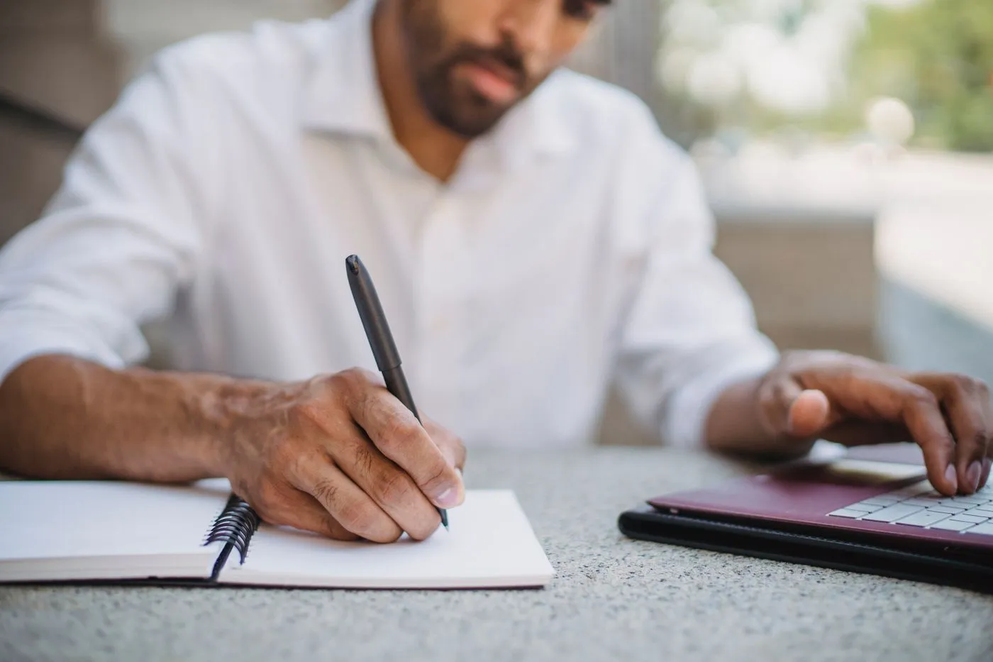 Une main prend des notes dans un carnet à côté d'un ordinateur portable
