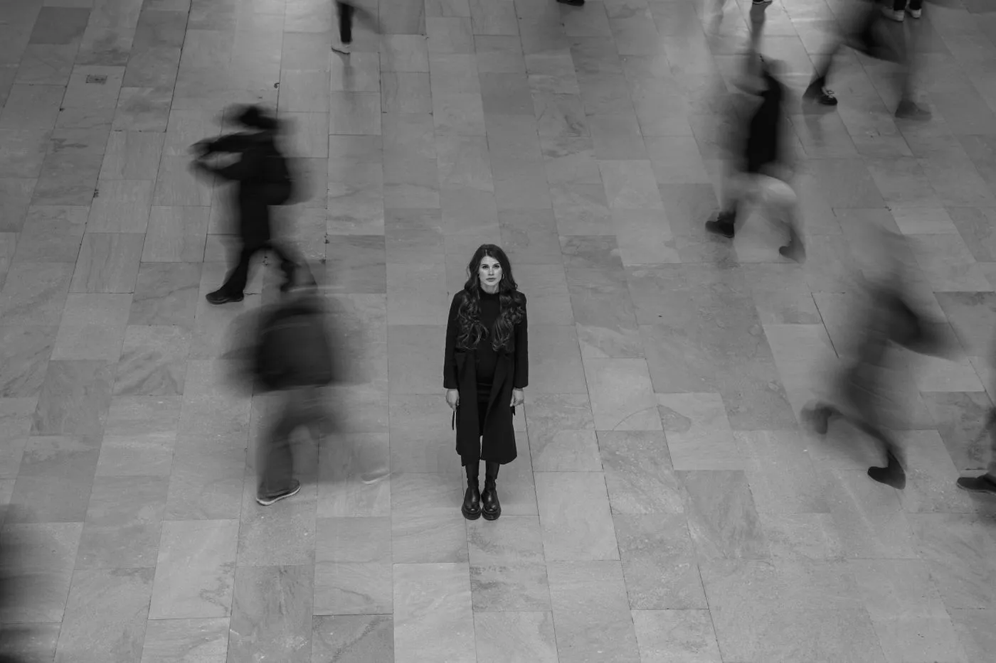 Une femme immobile au milieu d'une foule qui passe dans un hall
