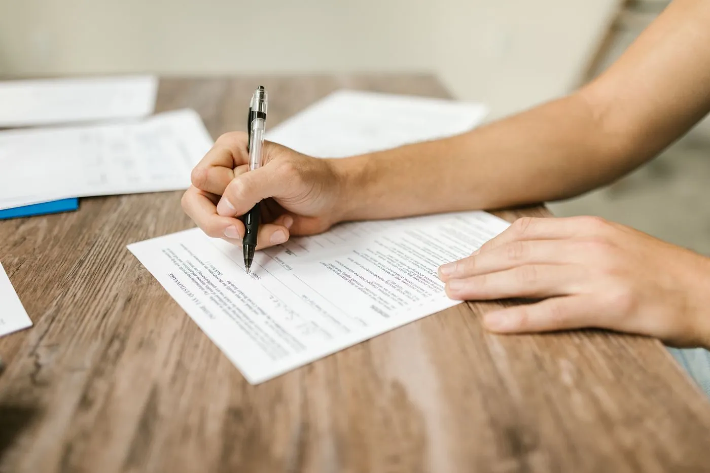 Une main remplit un formulaire au stylo sur une table en bois