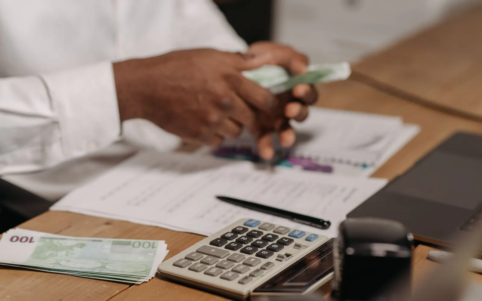 Des mains comptent des billets au-dessus d'un bureau